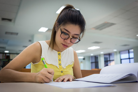 This is an image of a young woman writing an essay. She is in a library and appears to be in deep concentration.