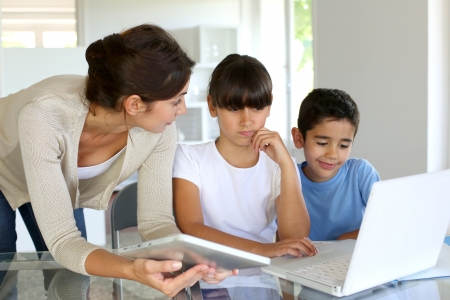 This is a picture of a teacher holding a tablet and helping two students who are working on a computer.