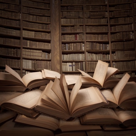 This is a picture of an old library with a bunch of antique books on the floor. They are open and the pages are leafing. No person is in the picture.